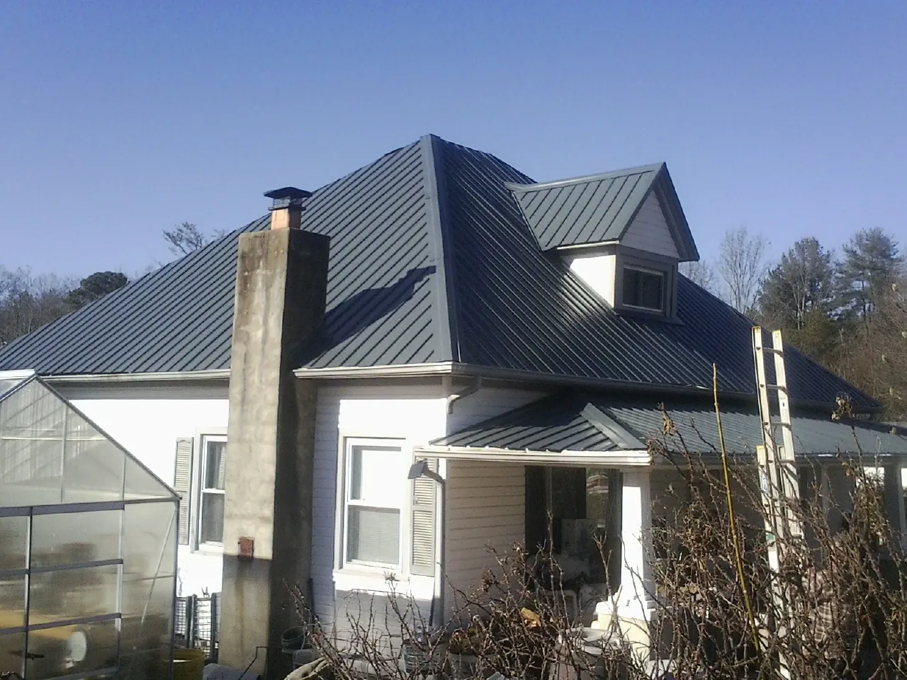 Dark blue standing seam metal roof on a white farmhouse with dormer — Slate & Tile Roof Repair by Roofing Brothers in Hay Springs