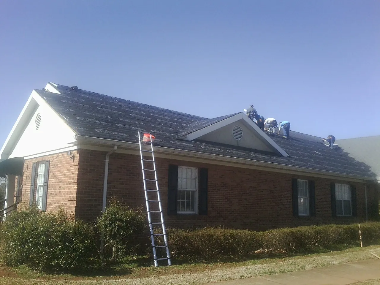 Crew tearing shingles off a brick ranch roof with a ladder set — Emergency Roof Repair work by our crew in Hay Springs