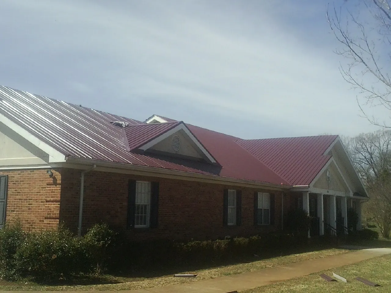 Red metal roof with gabled entries on a long brick building, from a Hail Damage Roof Repair job in Hay Springs