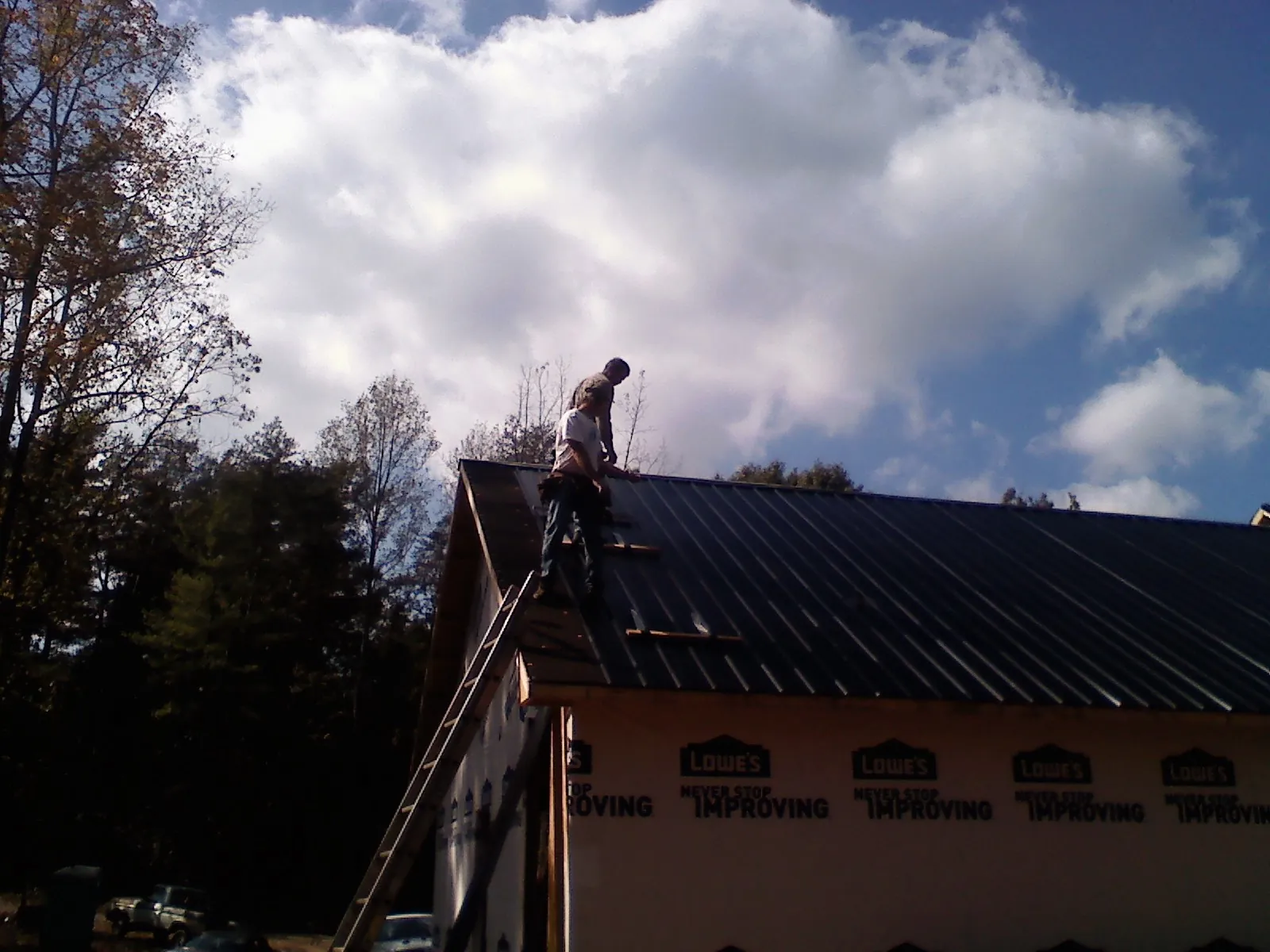 Roofer fastening dark metal panels high against a cloudy sky, from a Roof Inspection job in Hay Springs