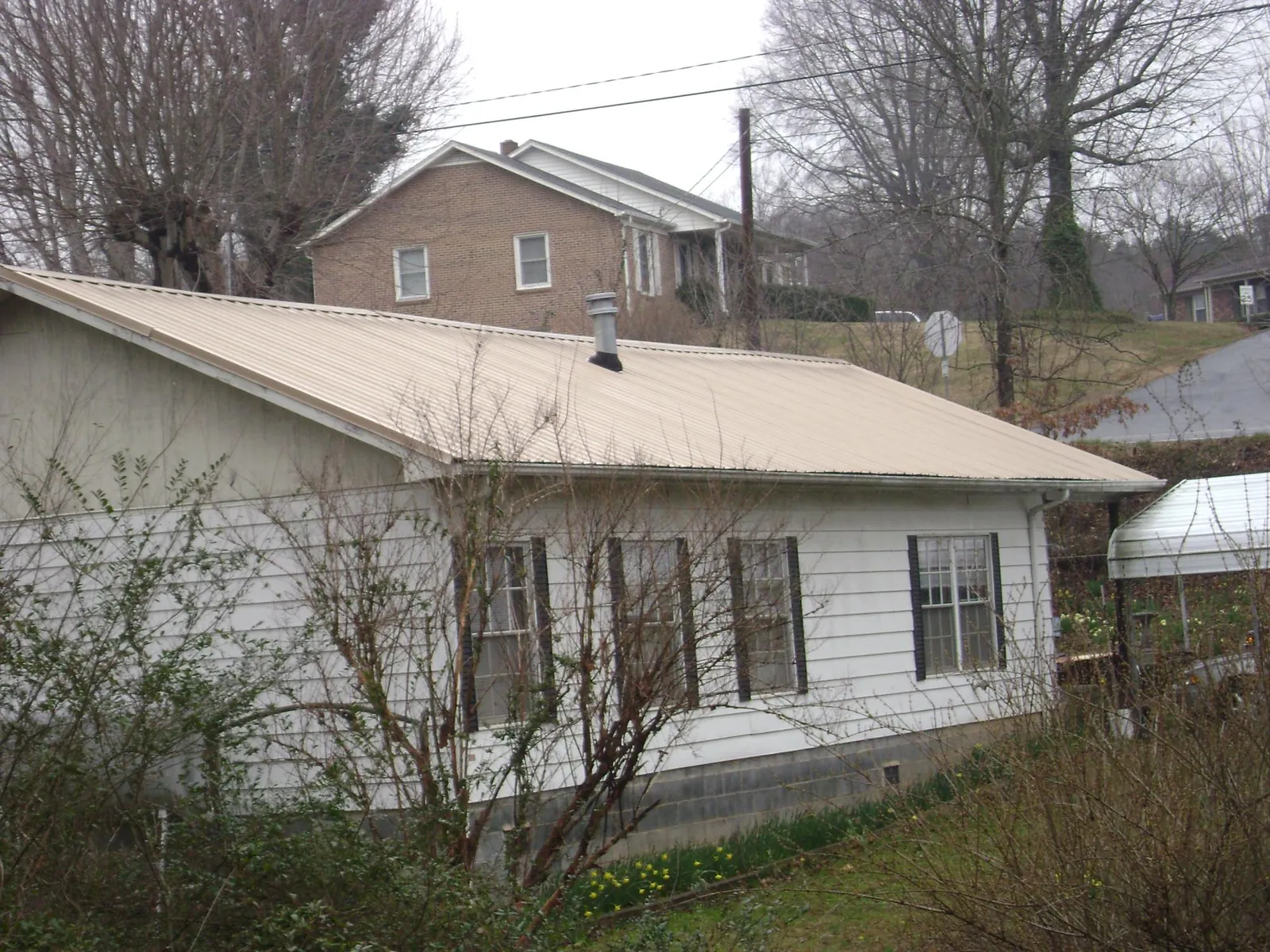 Tan metal roof on a white sided house set into a hillside — Commercial Roofing by Roofing Brothers in Hay Springs