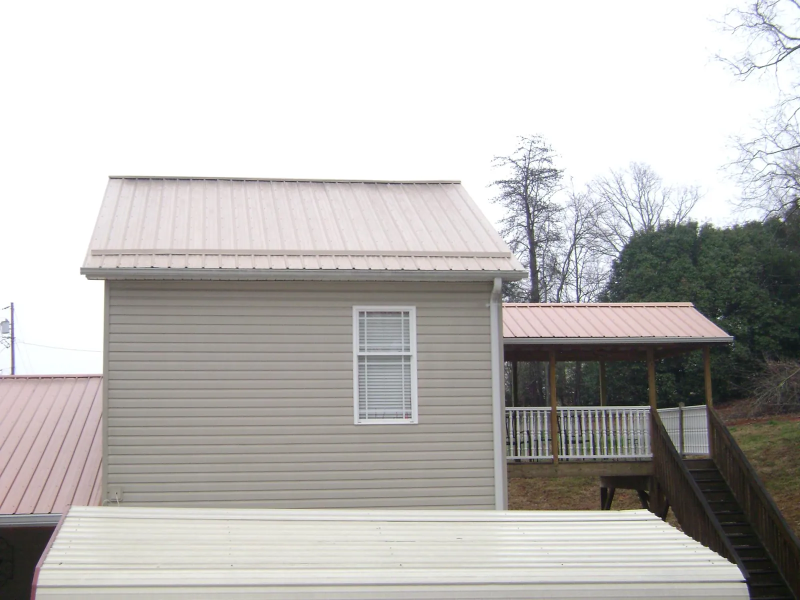 Tan metal roofs on a two story addition and attached porch, from a Roof Replacement job in Hay Springs